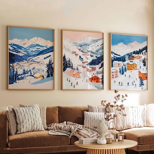 May include: Three framed illustrations of a snowy mountain village with colorful houses and skiers. The illustrations are in a modern style with a minimalist aesthetic.