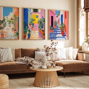 May include: A brown sectional sofa with striped throw pillows and a wooden coffee table in front of it. Three colorful paintings of a street scene with vibrant colors and potted plants hang on the wall behind the sofa.