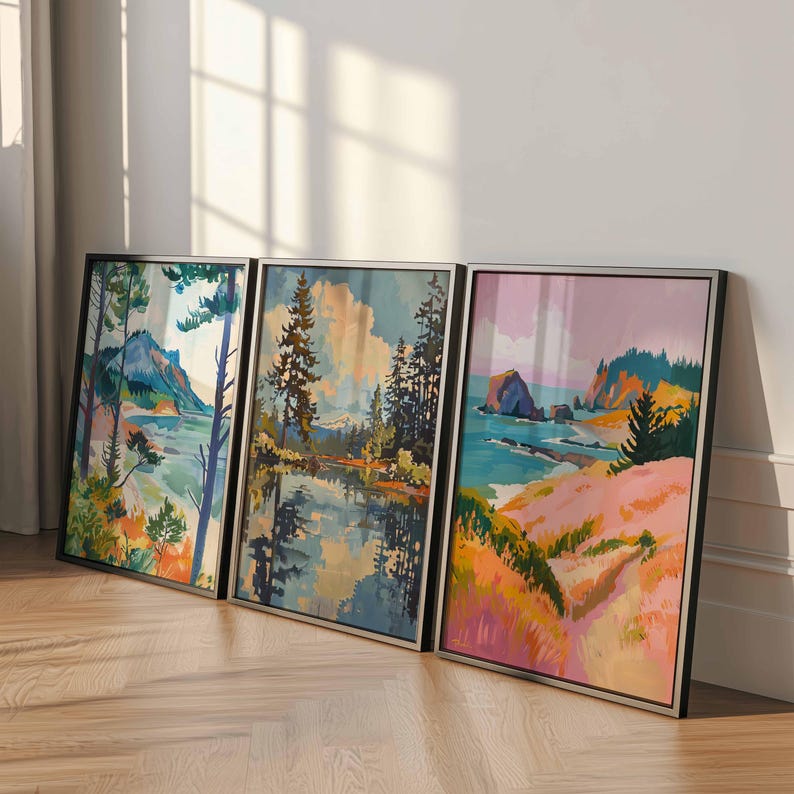May include: Three framed landscape art prints. Each print features a colorful coastal or forest scene with trees, water, and mountains. The frames are black with silver borders, and the art has a watercolor style.