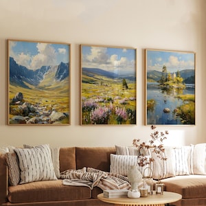 May include: Three framed landscape paintings with wooden frames. The paintings depict scenic views of mountains, fields, and a lake with a castle. The colour palette includes blues, greens, yellows, and pinks, creating a serene atmosphere.