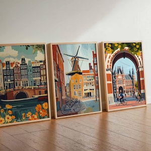 Pu&ograve; includere: Tre stampe artistiche incorniciate raffiguranti scene di Amsterdam. L'opera presenta edifici colorati, canali, mulini a vento e ciclisti. Le stampe sono esposte su un pavimento in legno contro un muro bianco, con un tema di viaggio.