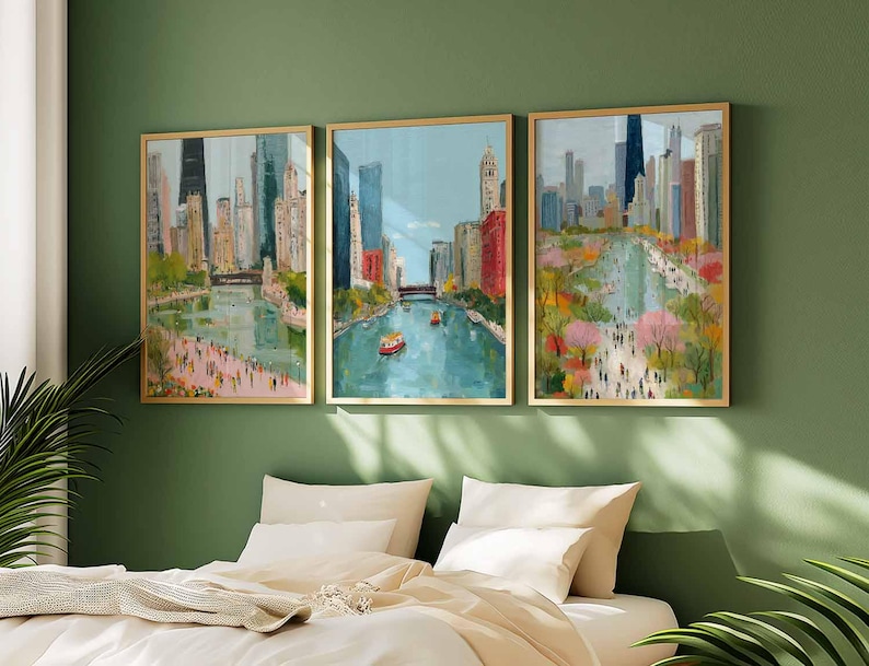 May include: Three framed art prints depicting a cityscape with a river and tall buildings. The artwork features a colorful, impressionistic style with gold frames. The paintings are displayed above a bed with white bedding, against a green wall.