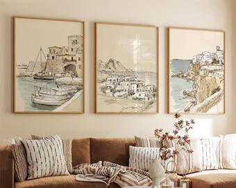 May include: Three framed wall art prints featuring ink and watercolor sketches of coastal Mediterranean scenes. The left print shows boats in a harbor, the center shows a hillside village, and the right shows a cliffside town by the sea.