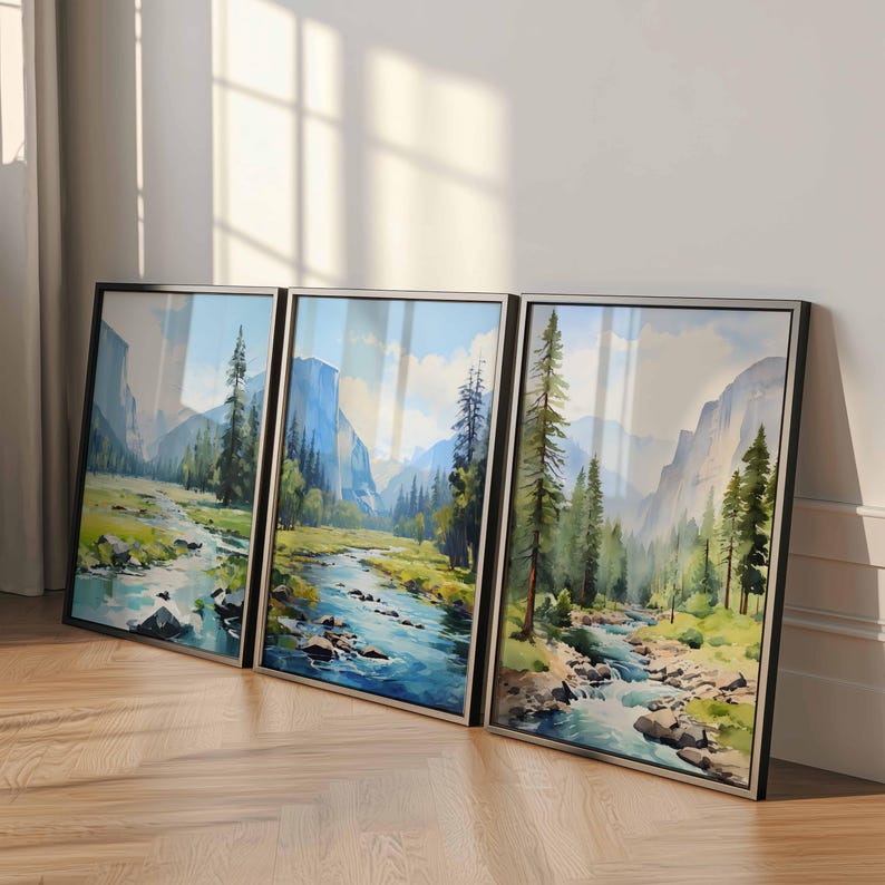 May include: Three framed landscape art prints featuring a river flowing through a valley with mountains and trees. The artwork has a watercolor style with blue, green, and brown tones. The frames are black with silver trim.