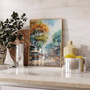 May include: A framed watercolor painting of a street scene in a city. The painting features a street lined with buildings and trees, with people walking along the street. The painting is framed in a gold frame.