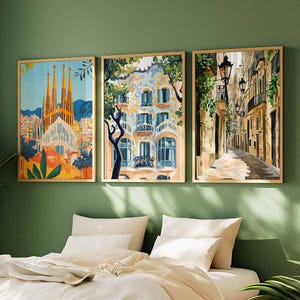 May include: Three framed art prints depicting architectural scenes. The prints feature a cathedral, a building with balconies, and a narrow street with streetlights. The frames are gold-colored, and the artwork is displayed on a green wall above a bed.