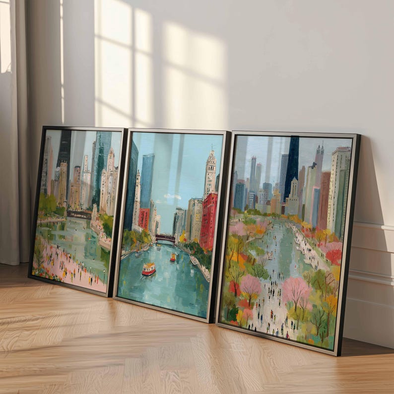 May include: Set of three framed cityscape art prints. The artwork depicts a river scene with buildings, boats, and people. The color palette includes blues, greens, pinks, and browns. The frames are black.