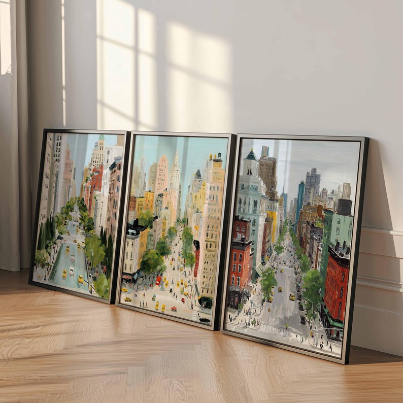 May include: Three framed cityscape art prints. The artwork depicts a vibrant street scene with tall buildings, yellow taxis, and pedestrians. The color palette includes shades of beige, red, green, and blue. The frames are black with silver trim.