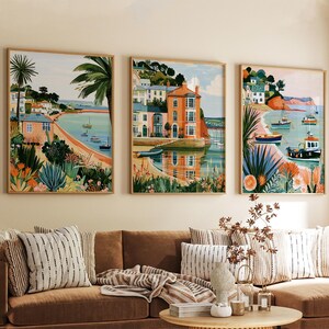 Pode incluir: Um conjunto de três impressões de arte de parede emolduradas retratando cenas costeiras com casas coloridas, palmeiras e barcos na água. As pinturas apresentam tons vibrantes de laranja, azul e verde, exibindo uma paisagem à beira-mar.