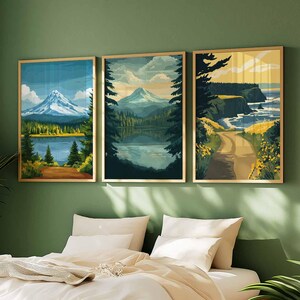 May include: Three framed landscape art prints. The prints depict mountain scenes, lakes, and coastal views. The artwork features a color palette of blues, greens, and yellows, with gold frames. The art is displayed above a bed with white bedding and pillows.