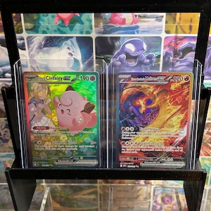 May include: A black display stand holding two trading cards. The left card features a pink Clefairy with the text "Li Clefairy EX 190". The right card shows a fiery Moltres with the text "Tum Moltres EX 220".