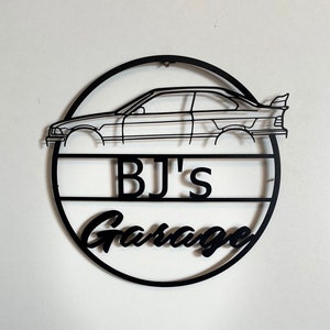 Puede incluir: Un letrero de metal negro con la silueta de un coche y el texto "BJ's Garage".