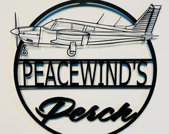May include: Black metal wall decor featuring a silhouette of a small airplane with the text "PEACEWIND'S Perch" in a circle.