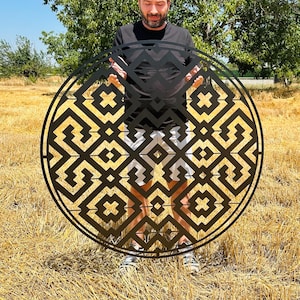 May include: A large, circular, black metal wall art piece featuring a complex, symmetrical geometric pattern with interconnected squares, zig-zag lines, and diamond shapes, creating an openwork design that allows light to pass through the structure.