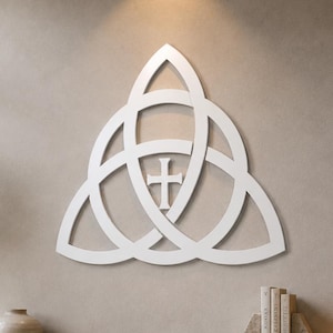 May include: A white wall-mounted decor piece featuring a triquetra knot design with a central cross. The object is constructed from interconnected curved lines forming a triangular shape, displaying a clean, solid white finish throughout its structure.