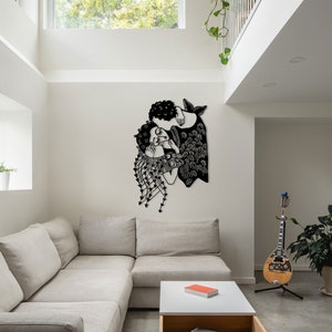 Op de afbeelding: Een zwart metalen wandkunstwerk dat twee figuren in een omhelzing afbeeldt. Het kunstwerk heeft ingewikkelde uitgesneden details, waaronder gestileerd haar, kleding en decoratieve elementen. Het stuk is bevestigd aan een witte muur in een moderne woonkamer.