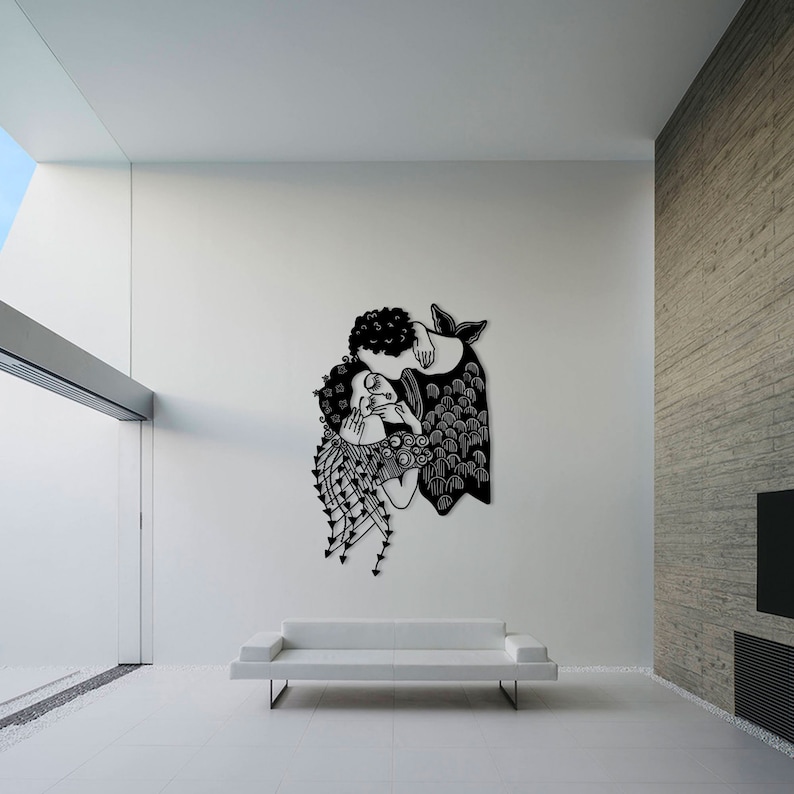 Op de afbeelding: Zwarte metalen wandkunst met twee figuren die elkaar omarmen. Het kunstwerk heeft ingewikkelde details, waaronder vloeiend haar en kleding met patronen. De figuren staan tegen een witte muur, wat een opvallend contrast cre&euml;ert. Een decoratief element voor een modern interieur.