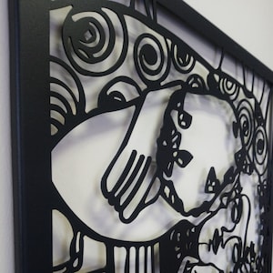 Op de afbeelding: Zwarte metalen wandkunst met een uitgesneden ontwerp van een gestileerd gezicht en draaiende patronen.