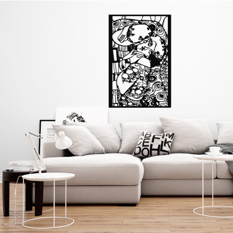 Op de afbeelding: Zwart-witte wandkunst die een knuffelend stel afbeeldt. De kunst is ingelijst in een zwart frame en hangt aan een witte muur boven een witte bank.