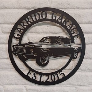 Puede incluir: Se&ntilde;al de metal negro con la silueta de un coche cl&aacute;sico y el texto "Garrido Garage Est. 2015".