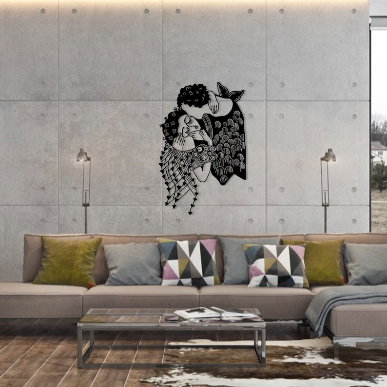 Op de afbeelding: Een zwart metalen wandkunstwerk dat twee figuren in een omhelzing afbeeldt. Het kunstwerk heeft ingewikkelde uitgesneden details, waarbij een figuur een zeemeerminstaart lijkt te hebben. Het is gemonteerd op een betonnen muur boven een bank met kleurrijke kussens.