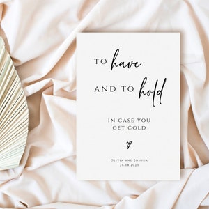 May include: A white card with black calligraphy that reads "To have and to hold in case you get cold."  The card also includes a small heart and the text "Olivia and Joshua 26.08.2021".