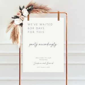 May include: White wedding sign with a copper stand. The sign says "We've waited 634 days for this party accordingly. Welcome to our wedding Jessica and David 26th March 2023".