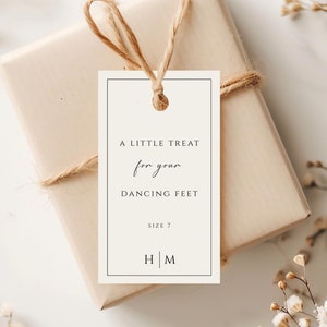 Puede incluir: Una etiqueta de regalo blanca con texto negro que dice "A little treat for your dancing feet, size 7, H | M". La etiqueta está atada con un cordel a una caja de regalo marrón.