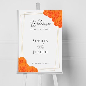 May include: A white wedding welcome sign with a gold frame and orange roses. The sign reads "Welcome to our wedding, Sophia and Joseph, 17th December 2023".