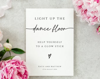 May include: White sign with black text that reads "Light up the dance floor. Help yourself to a glow stick. ♡ Katie and Matthew 27th August 2024".