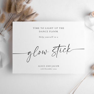 May include: White card with black text that reads "Time to light up the dance floor. Help yourself to a glow stick. Alice and Jacob 17th December 2025".