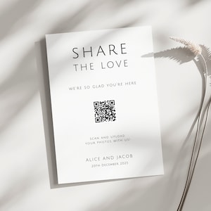 Puede incluir: Tarjeta blanca con texto negro que dice "Comparte el amor" y "Estamos tan contentos de que estés aquí". Debajo del texto hay un código QR en blanco y negro. El texto "¡Escanea y sube tus fotos con nosotros!" está debajo del código QR. El texto "Alice y Jacob 20 de diciembre de 2025" está en la parte inferior de la tarjeta.