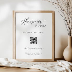 Op de afbeelding: Een ingelijst bord met de woorden "Honeymoon Fund" in elegant schrift. Hieronder staat "Scan here to make our day" met een QR-code. De onderkant van het bord zegt "Thank you from the newlyweds" en de namen Sophia en Joseph, met de datum 19 december 2025.