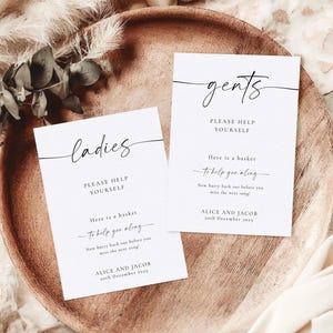 May include: Two white signs with black text, one for "ladies" and one for "gents". Both signs say "Please help yourself" and "Here is a basket to help you along". The signs also include the names "Alice and Jacob" and the date "20th December 2021".