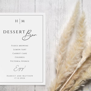 May include: A white sign with black text announcing a dessert bar with the names "Harriet and Matthew" and the date "17.12.2024". The sign lists the following desserts: Fudge Brownie, Lemon Tart, Carrot Cake, Churros, and Victoria Sponge.