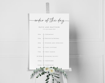 May include: A white wedding order of the day sign with black text. The sign lists the wedding events with times, including the ceremony, photos and drinks, dinner and speeches, cake cutting, first dance, evening buffet, fireworks, and carriages.