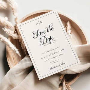 Op de afbeelding: Een crèmekleurige "Save the Date" kaart met zwarte kalligrafie en een zwarte rand. De kaart bevat de namen Alice en Richard, de datum 14 november 2026 en de locatie HolmeWood Hall, Cambridge. De kaart ligt op een houten dienblad.