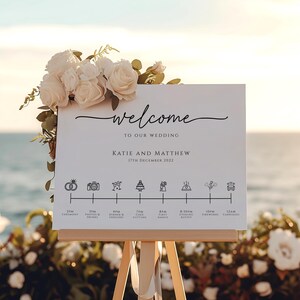 May include: A white wedding welcome sign with black text and icons. The sign says "Welcome to our wedding Katie and Matthew 17th December 2022".