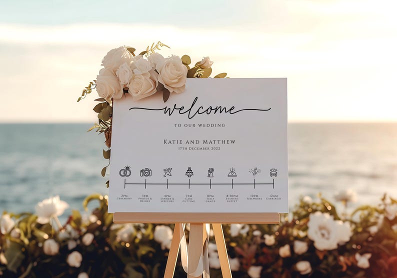 May include: A white wedding welcome sign with black text and icons. The sign says "Welcome to our wedding Katie and Matthew 17th December 2022".