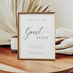 Może przedstawiać: Oprawiony znak ze złotą obwódką, wyświetlający słowa "PLEASE SIGN OUR Guest Book" w eleganckim skrypcie. Znak zawiera również tekst "THANK YOU FOR SHARING THIS SPECIAL DAY WITH US" oraz imiona "SOPHIA AND JOSEPH" z datą "19TH DECEMBER 2025".