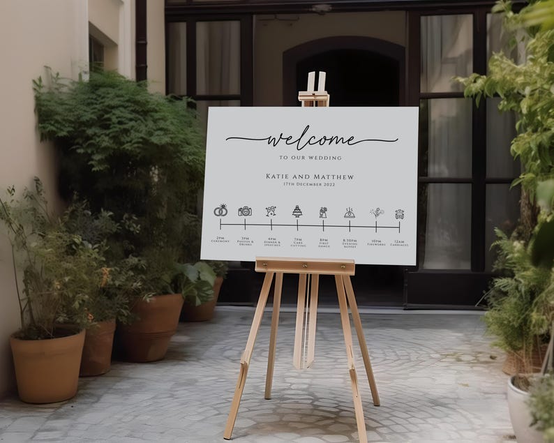 May include: A white welcome sign with black text and icons for a wedding. The sign says "Welcome to our wedding Katie and Matthew 17th December 2023". The icons represent different parts of the wedding day, such as the ceremony, photos, and dinner.