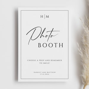 May include: A black and white photo booth sign with the text "Photo Booth" and the initials "H|M". The sign also includes the text "Choose a prop and remember to smile!" and "Harriet and Matthew 17.12.2024".