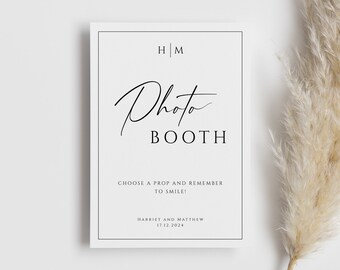May include: A black and white photo booth sign with the text "Photo Booth" and the initials "H|M". The sign also includes the text "Choose a prop and remember to smile!" and "Harriet and Matthew 17.12.2024".