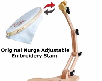 May include: A wooden embroidery stand with adjustable arms and a rotating clamp for holding embroidery hoops. The stand is made of natural wood and has a light brown finish. The clamp is black and has a small knob for tightening. The stand is designed to hold embroidery hoops of various sizes.