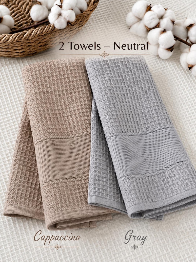 May include: Two folded waffle-weave towels, one in a light brown cappuccino color and one in a light gray color. The text 2 Towels - Neutral is centered above the towels, with the word Cappuccino below the brown towel and Gray below the gray towel.