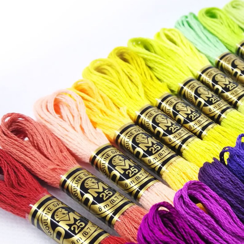 Op de afbeelding: Een regenboogassortiment van borduurgaren spoelen, elk met het label "DMC 25" en "8 m (8,7 yd)".