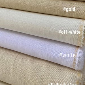 May include: Close-up of folded fabric samples in cream, gold, off-white, white, and light beige. The fabric has a woven texture. The colors are labeled with hashtags: #cream, #gold, #off-white, #white, and #light beige.