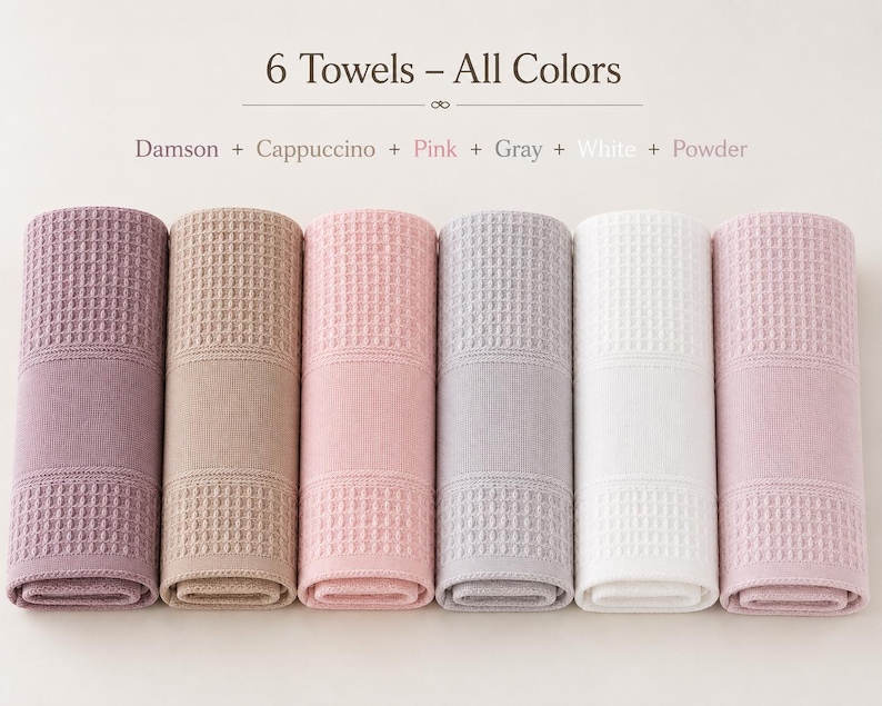May include: Six rolled towels featuring a waffle-textured pattern and a smooth band. The text reads 6 Towels &ndash; All Colors, Damson + Cappuccino + Pink + Gray + White + Powder. The colors are dark purple, tan, light pink, light gray, white, and pale pink.