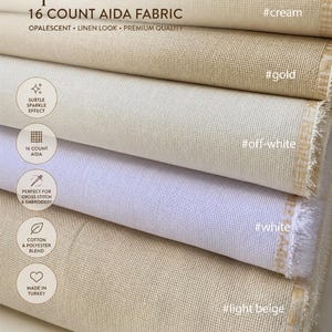 May include: Close-up of stacked rolls of 16 count Aida fabric in various shades, including cream, gold, off-white, white, and light beige. The fabric has a linen look and is opalescent. Text on the image reads "Sparkle" and "Perfect for cross stitch & embroidery."