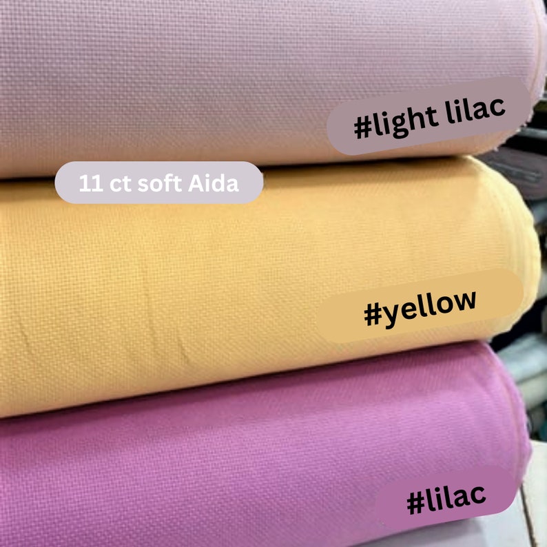May include: Three rolls of 11 count soft Aida fabric in lilac, yellow, and light lilac.  The fabric is a woven cotton fabric with a small grid pattern.  The fabric is commonly used for cross stitch and other needlework projects.